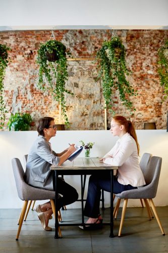 Side view of employer with document and young applicant looking for job in cafe